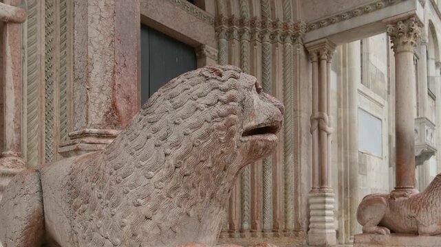 Modena, italy, april 12, 2026. Point of view walking shot revealing the romanesque architecture and marble lion statue at the entrance of modena cathedral in italy