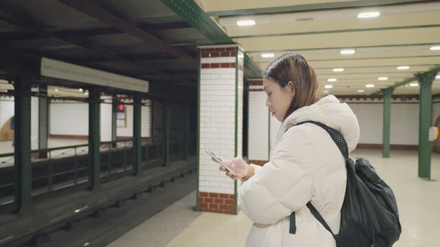 A commuter waits at a subway station, engaged with a mobile device. The station features modern design elements and empty platforms, creating a quiet atmosphere for passengers.