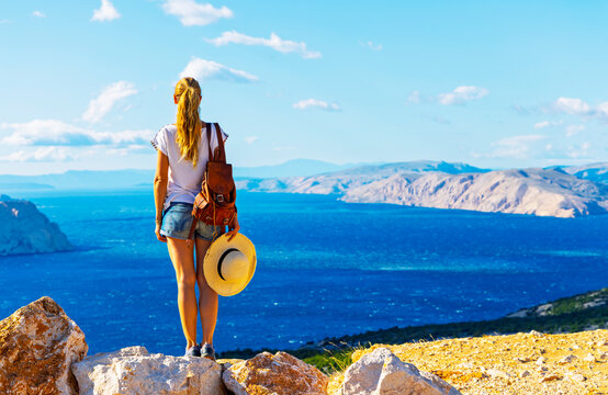 woman traveler with backpack and straw hat looking at the sea summer vacation and freedom concept