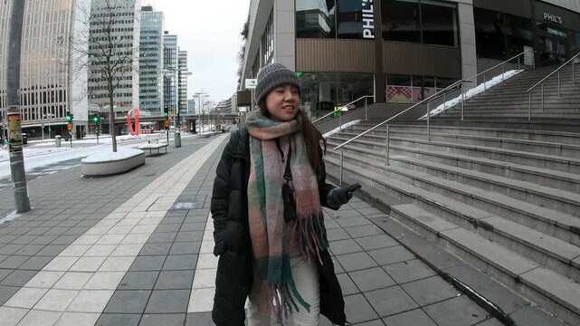 A woman dressed warmly walks through a modern cityscape with urban architecture and winter conditions, showcasing the hustle and bustle of city life during colder months.