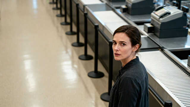 [Young woman] [with serious mood] [standing in a waiting line against a professional background]