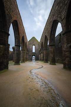 View of the ancient stone ruins of Pointe Saint-Mathieu abbey with gothic arches and a winding water trail on the ground in Plougonvelin, Brittany, France.
