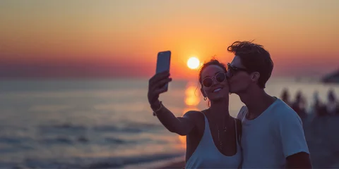 Happy young couple, taking a selfie on a beach at sunset, kissing man and smiling woman on summer vacations, ocean panoramic background with copy space © Delphotostock