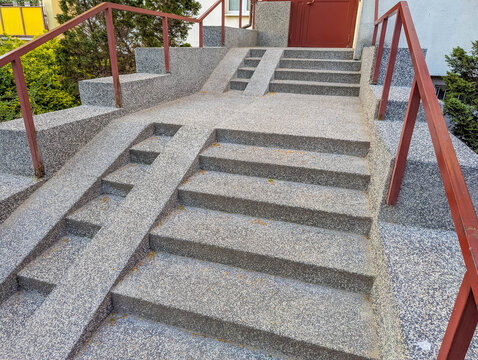 Warsaw, Poland, April 17, 2026. Close up of outdoor stone stairs and a concrete ramp for strollers and wheelchairs with red railings. High quality photograph.