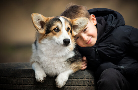 Affectionate boy leaning his head against his Corgi puppy.