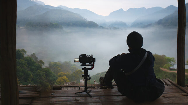 Solo traveler filming misty mountain landscape at sunrise in Thailand. Cinematic introvert lifestyle, content creator, peaceful solitude and nature exploration concept