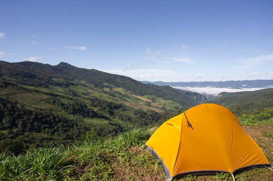 Bright yellow camping tent on mountain viewpoint in Thailand with panoramic green valley and blue sky. Outdoor adventure, travel lifestyle and nature background concept