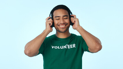 Fototapeta premium Studio, volunteer and man with headphones, charity and listening to music with subscription on break. Blue background, humanitarian and happy person with tech for playlist, ngo and streaming audio