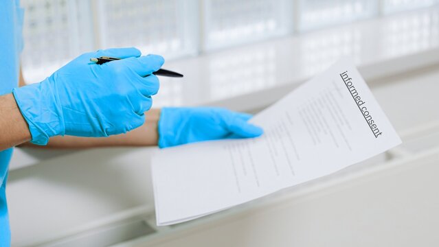 Healthcare professional wearing gloves holding informed consent document. Concept of patient agreement, medical ethics, legal approval, and healthcare documentation.