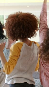 Vertical video: Raising arms central woman in raglan leading friends social dancing at home, sofa