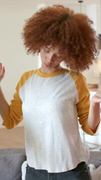Dancing woman in white raglan reacting to offscreen elbow, folding arms in living room with sofa