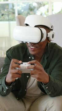 Vertical video: Playing man wearing green shirt pressing controller with white VR headset for fun