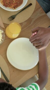 Vertical video: Reaching boy, dad in red holding hand at table before meal with juice, copy space