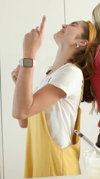 Vertical video: Singing women in yellow and red shirts miming while baking in kitchen using spoons