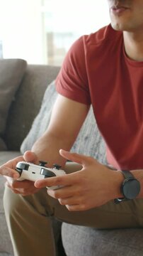 Vertical video: Settling man in red tee on sofa tuning white gamepad and raising VR headset to play