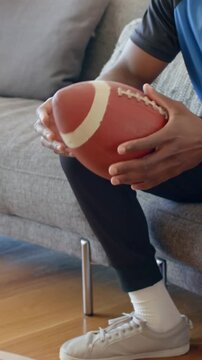 Vertical video: Lifting from lap, man in blue shirt rotating football laces to check grip on sofa