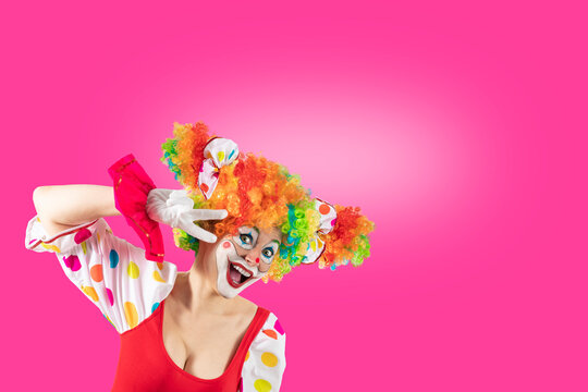 Funny female clown, woman entertainer dressed as a colorful Joker in a suit and wig, with clown whiteface makeup