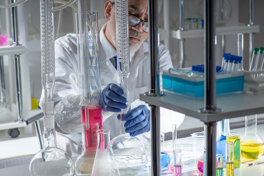 Experienced senior scientist analyzing chemical samples among glass flasks and test tubes  in a modern laboratory. Concept of professional research, chemistry expertise, scientific methodology.