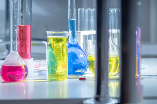Chemical laboratory background with glassware, measuring cylinders and colorful solutions on table, science research concept, shallow depth of field and blur.