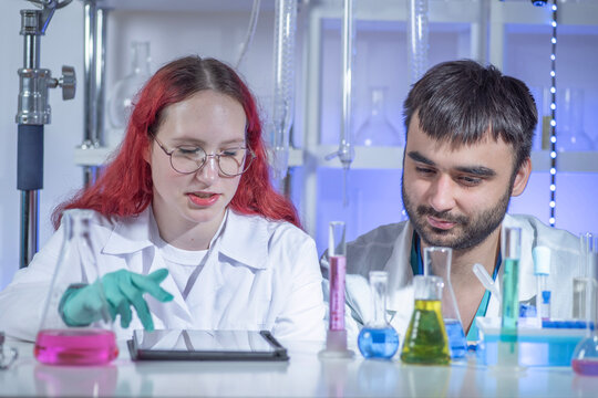 Young female lab technician working on a tablet while collaborating with male colleague in modern laboratory. Digital technology in chemistry research, teamwork, analysis and innovation concept.