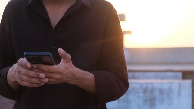 Close up of a man using a smartphone outdoors during the golden hour sunset