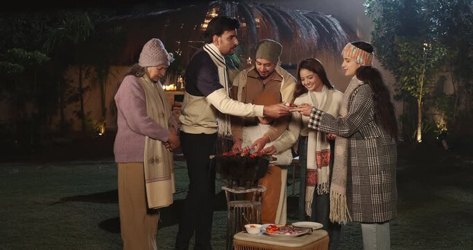 Indian happy mature adult female male speak share gossip enjoy winter cold have fun joy night outdoor garden place mom girl child kid talk with young man cook party food on barbecue spend quality time