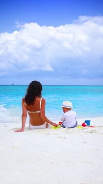A mother and her little baby son playing together in the sand of a beautiful beach with white sand and turquoise ocean