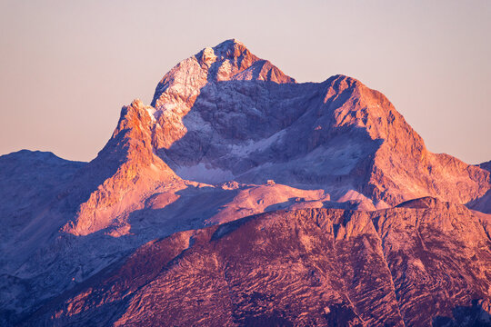 View of the majestic snow-dusted peak of Mount Triglav glowing under the warm light of a sunrise in Sorica, Skofja Loka, Slovenia.