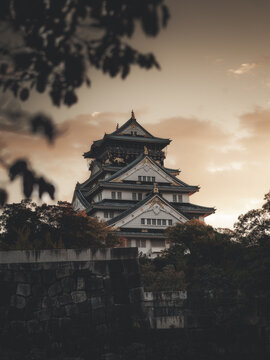 View of the historic Osaka Castle featuring multi-tiered white walls and golden ornaments against a sunset sky Japan.