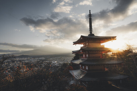 View of the Chureito Pagoda and Mount Fuji at sunset with golden light rays and the city skyline in Japan.