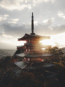 View of the Chureito Pagoda with a sunset flare and Mount Fuji in the background surrounded by autumn foliage in Japan.