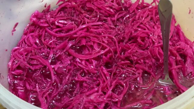 Bright pink sauerkraut in bucket, shop display with spoon, shredded cabbage mixed with beetroot, glossy brine sheen, plastic white