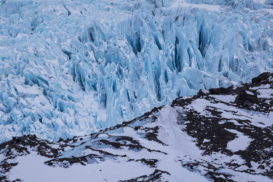 View of Falljokull glacier featuring jagged blue ice crevasses and deep fissures alongside rocky snow-covered terrain in Sveitarfelagid Hornafjordur, Iceland.