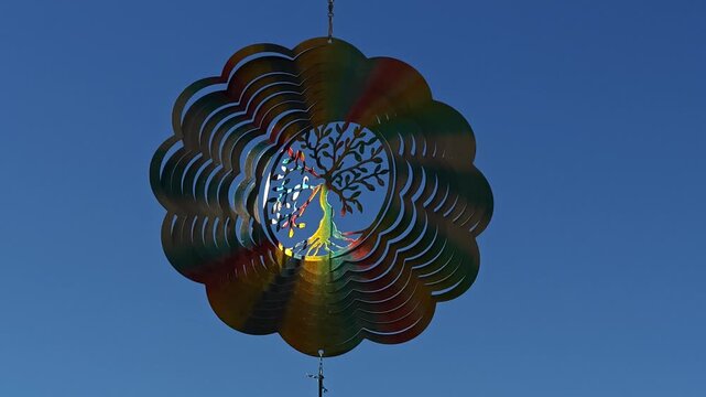 Metal Flower Wind Spinner Featuring Tree of Life Rotating in Gentle Breeze Against Blue Sky and White Clouds, Spiritual Garden Decor, Meditation Symbol, Peaceful Outdoor Wind Sculpture