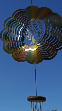 Metal Flower Wind Spinner Featuring Tree of Life Rotating in Gentle Breeze Against Blue Sky and White Clouds, Spiritual Garden Decor, Meditation Symbol, Peaceful Outdoor Wind Sculpture
