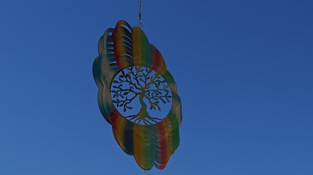 Metal Flower Wind Spinner Featuring Tree of Life Rotating in Gentle Breeze Against Blue Sky and White Clouds, Spiritual Garden Decor, Meditation Symbol, Peaceful Outdoor Wind Sculpture