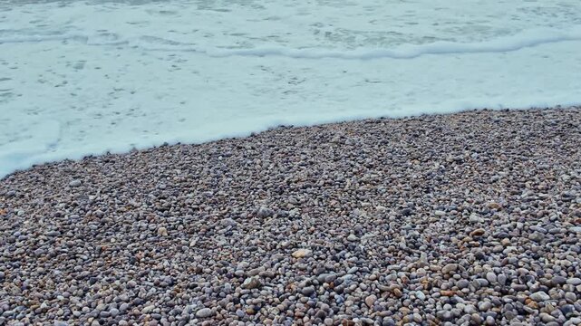 Powerful ocean waves crashing onto pebble shoreline creating dynamic foam and motion in coastal environment.