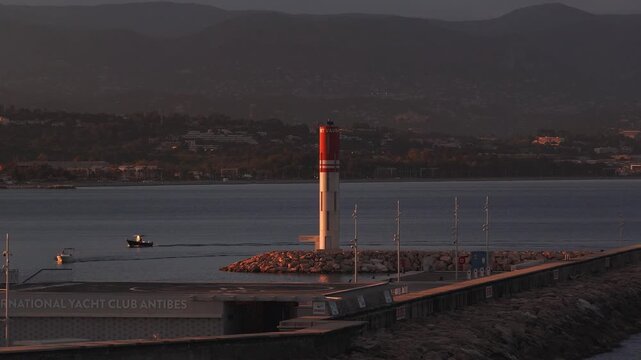 Aerial sunset view of Antibes, France, with breakwater and Port Vauban tower. Warm light skims jetty and boats as the camera pans, signage reads International Yacht Club Antibes.