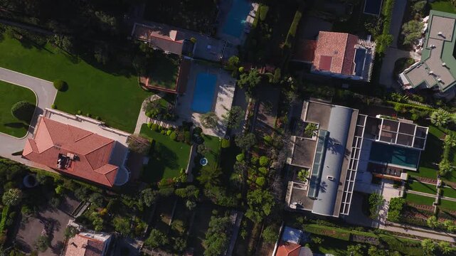 Aerial view over Antibes, France shows terracotta tiled villas, palms, cypress, pools, and hedged paths. The camera pans from top down to oblique in warm late light.