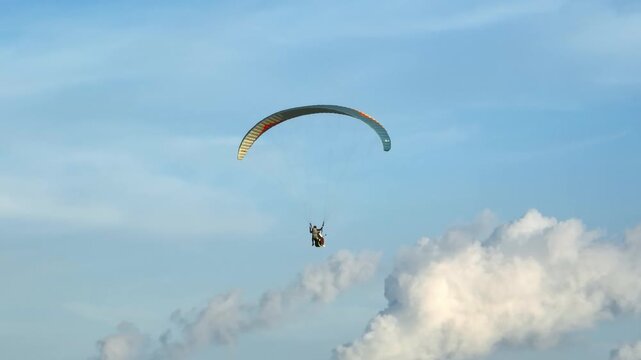 People enjoying a tandem paragliding flying experience, soaring through the blue sky with clouds in the background, representing freedom, adventure, and extreme sports tourism in Bali, Indonesia