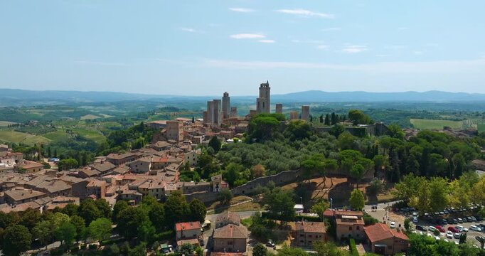 San Gimignano Italy ancient architecture drone shot. High density stone towers green forest landscape summer atmosphere. Aerial cityscape Tuscany region tourism landmark exploration heritage site.

