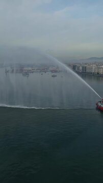 THESSALONIKI, GREECE - JANUARY 6, 2024 Vertical aerial drone shot of fireboats spraying water from cannons in the Thermaikos Gulf during the Epiphany celebrations at the city waterfront.