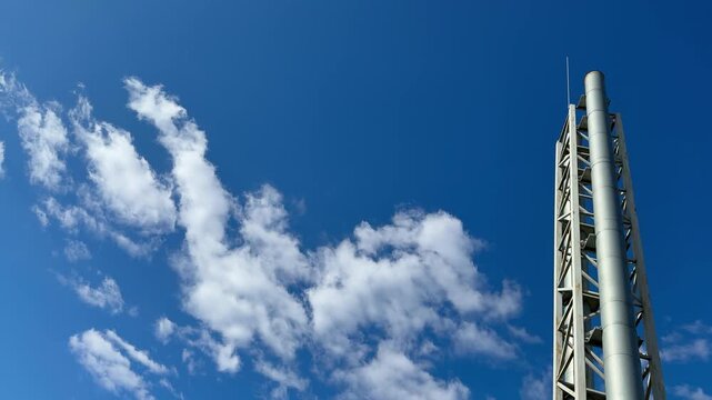 Steel heating pipe tower against sky narrow stainless column rises into vivid blue with drifting white clouds, visible lattice
