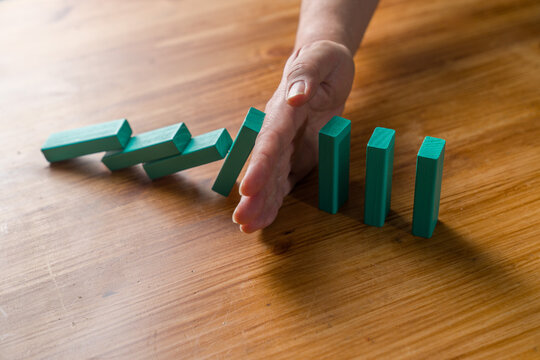 Hand stopping falling domino chain on wooden table risk control concept