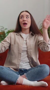 Portrait of trendy cheerful positive young woman having fun dancing and moving to rhythm, dabbing raising hands, making dub dance gesture sitting on sofa. lady at modern home living room apartment