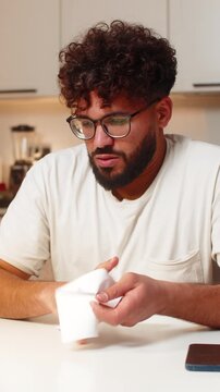 Arabian man at home reads utility bill crumples paper feels angry sighs then calms down. Young guy sitting at table smooths receipt plans to call support ask why charges are high then dials late.