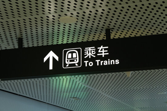 A bilingual directional sign in a modern station showing an arrow and a train icon with text "To Trains".