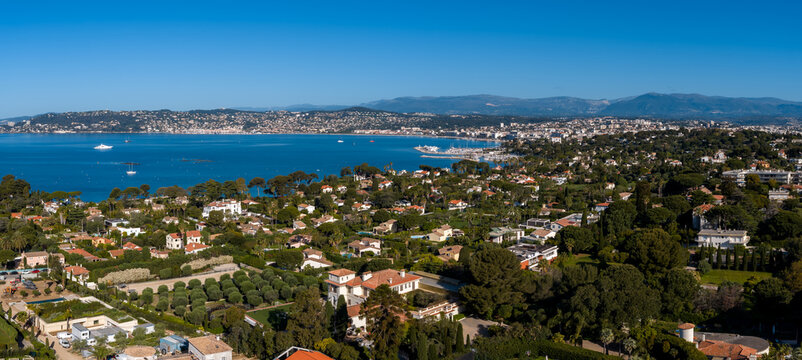 Aerial view of Antibes, France, shows Cap d Antibes, villas, gardens, and the Bay of Angels, with Alps on the horizon, yachts and sailboats, and terracotta roofs.