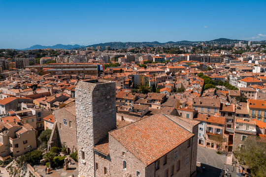 Aerial view of Antibes, France, with terracotta rooftops around the Musee Picasso at Chateau Grimaldi, modern city beyond, midday light, foothills and Riviera townscape.