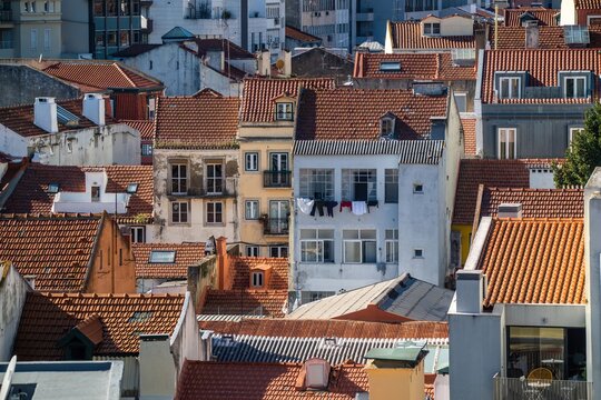 View of traditional buildings with orange terracotta tiled roofs and laundry hanging from a balcony in Lisbon, Lisbon, Portugal.